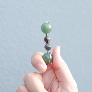 May include: A green and gray beaded necklace with a wire wrap design. The necklace is made with three beads, two green and one gray.