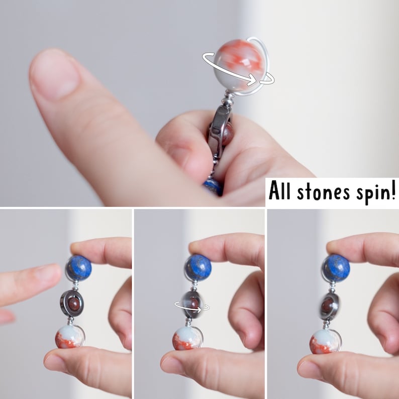 May include: A spinning, multi-colored, gemstone necklace with a silver chain. The necklace features three round stones: a blue lapis lazuli, a red jasper, and a white agate. The stones are connected by silver rings and spin freely. "All stones spin!" is written below the necklace.