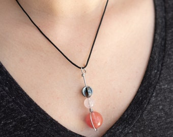 May include: A delicate necklace with a black cord and a silver pendant featuring a pink and clear stone with a silver wire wrap.