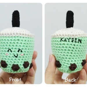 May include: A green crocheted boba tea cup with a black straw and brown boba pearls. The cup has a white crocheted lid and a smiling face. The back of the cup has the name "KAYDEN" embroidered on it.