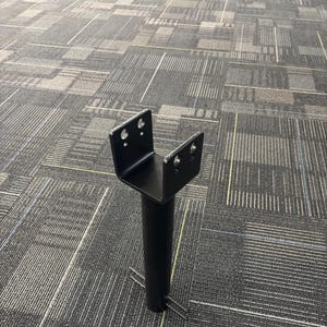 Könnte beinhalten: Ein schwarzer Metallpfosten mit U-förmiger Oberseite und zylindrischer Basis. Die Oberseite hat auf jeder Seite zwei Löcher. Zwei Metallstangen erstrecken sich von der Basis. Das Objekt befindet sich auf einem gemusterten Teppich.