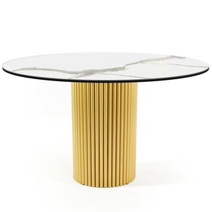 Pode incluir: Uma mesa de jantar redonda com tampo de mármore branco e base de metal dourado. A base é feita de uma série de tubos dourados verticais.
