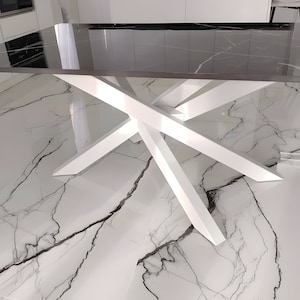 May include: A white dining table with a black glass top and a unique X-shaped base. The table is shown on a white marble floor.