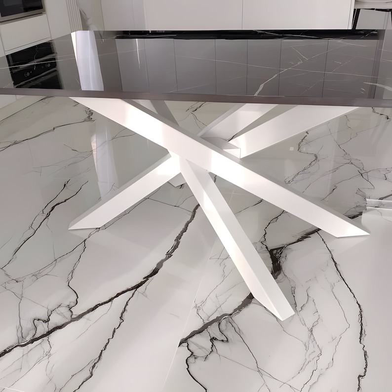 May include: A white dining table with a black glass top and a unique X-shaped base. The table is shown on a white marble floor.
