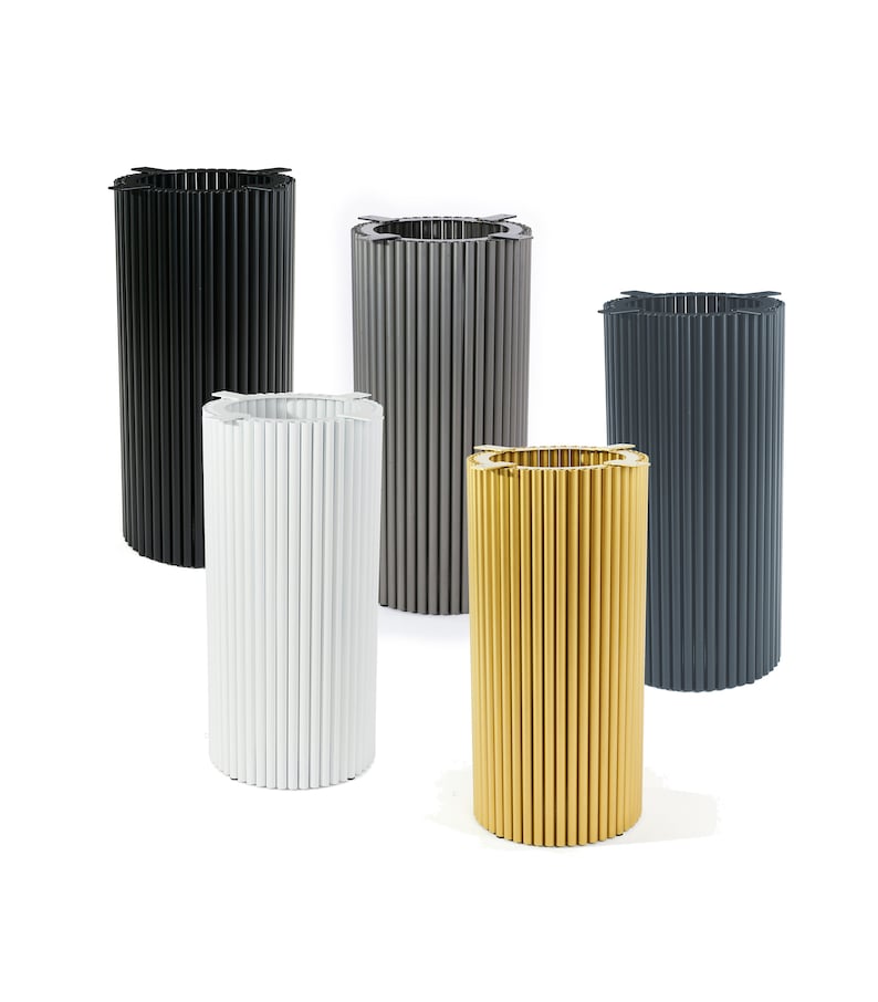 May include: Five cylindrical metal planters in different colors: black, gray, white, gold, and dark gray. The planters have a ribbed design and are arranged in a row.
