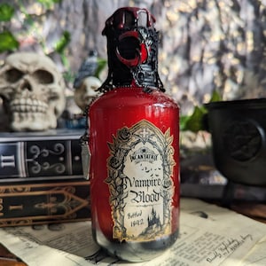 May include: A decorative glass bottle filled with red liquid, labeled "Incantatrix Vampire Blood, Bottled 1892." The bottle has a black and red ornate stopper and a silver chain. The background includes books and a skull.