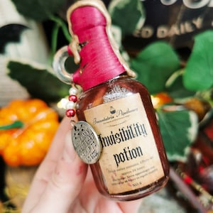 Könnte beinhalten: Kleine, braune Zaubertrankflasche mit rotem Wachssiegel und dekorativem Anhänger. Das Etikett trägt die Aufschrift "Invisibility Potion". Die Flasche ist Teil einer thematischen Sammlung, möglicherweise für Halloween- oder Fantasy-Enthusiasten.