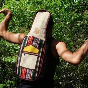 Könnte beinhalten: Eine Person trägt eine braune und mehrfarbige Gitarrentasche mit einer gelben Tasche. Die Tasche ist aus gewebtem Stoff und hat einen braunen Lederbesatz.