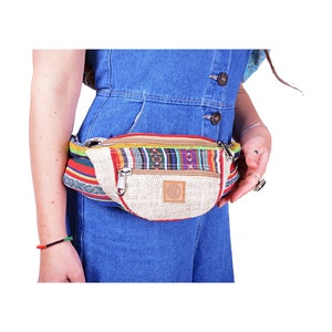 May include: A beige hemp fanny pack with a colourful woven strap and a zipper closure. The bag has a small brown logo on the front.