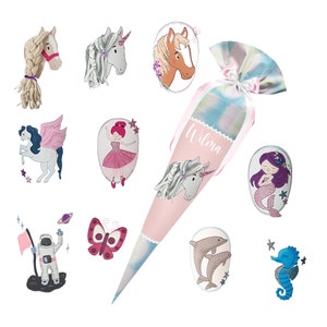 May include: A pink and blue school cone with the name "Wilma" written on it. The cone is decorated with a unicorn, a mermaid, a butterfly, a dolphin, a seahorse, a ballerina, and a unicorn with wings.