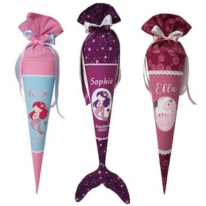 Puede incluir: Tres conos escolares rosas y morados con diseños de sirena y dinosaurio. Los conos están decorados con estrellas, puntos y encaje. Los conos están personalizados con los nombres "Rosa", "Sophia" y "Ella".