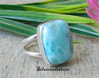 Könnte beinhalten: Ein silberner Ring mit einem quadratischen, hellblauen Edelstein. Der Edelstein hat ein wirbelndes, marmoriertes Muster.