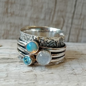 May include: A silver spinner ring with three stones. The ring has a textured band with a floral design. The stones are a light blue, a white, and a light blue-green.