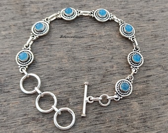 May include: A silver bracelet with a toggle clasp and blue gemstone accents. The bracelet has a delicate chain with round, ornate settings for each stone.