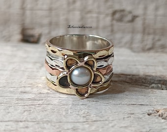 May include: A silver, copper and brass ring with a spinning flower design and a pearl in the centre.