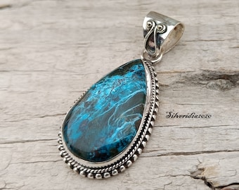 Può includere: Un ciondolo a forma di lacrima con una pietra preziosa blu e verde incastonata in argento. Il ciondolo ha un bordo perlato e un'anellina in argento.