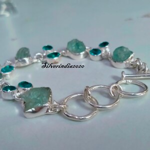Puede incluir: Un brazalete de plata con cierre de palanca presenta un dise&ntilde;o de cadena con m&uacute;ltiples piedras preciosas azul aguamarina. Las piedras preciosas tienen una forma irregular y un aspecto &aacute;spero y natural. El brazalete est&aacute; acentuado con piedras preciosas m&aacute;s peque&ntilde;as, redondas, azul turquesa.