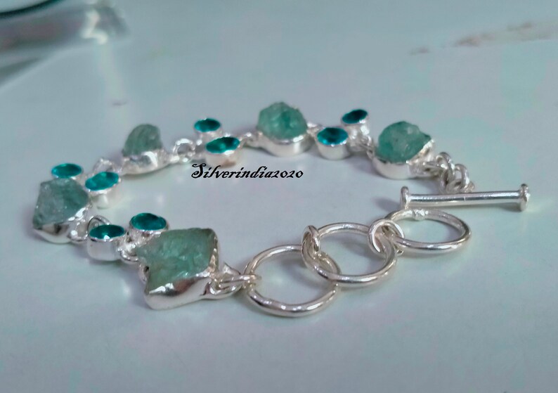 Puede incluir: Un brazalete de plata con cierre de palanca presenta un dise&ntilde;o de cadena con m&uacute;ltiples piedras preciosas azul aguamarina. Las piedras preciosas tienen una forma irregular y un aspecto &aacute;spero y natural. El brazalete est&aacute; acentuado con piedras preciosas m&aacute;s peque&ntilde;as, redondas, azul turquesa.