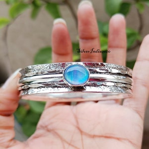 Peut inclure: Un bracelet en argent martelé avec une pierre précieuse bleu irisée. Le bracelet est composé de plusieurs bandes superposées.