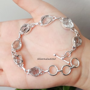 Puede incluir: Una pulsera de plata con piedras preciosas claras de forma irregular. Las piedras están unidas por una cadena de plata y engastadas en biseles de plata. La pulsera tiene un cierre de palanca. El texto "Silverindia2020" es visible.