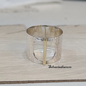 Puede incluir: Un anillo de plata con textura martillada y un acento de barra de oro. El anillo tiene un dise&ntilde;o recortado en el centro.