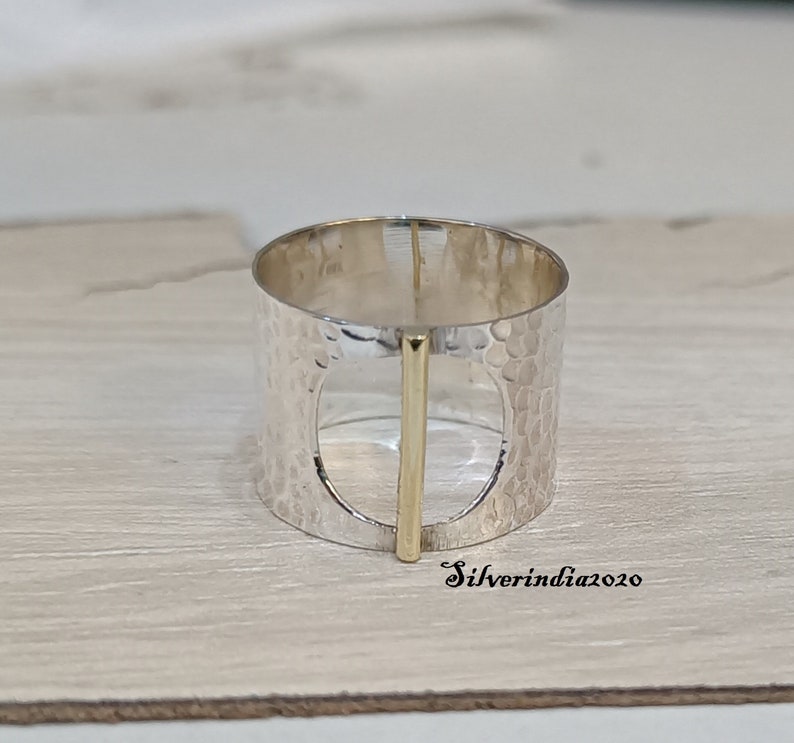 Puede incluir: Un anillo de plata con textura martillada y un acento de barra de oro. El anillo tiene un dise&ntilde;o recortado en el centro.