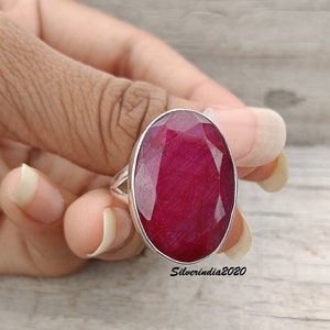 Pode incluir: Anel de prata com uma grande gema de rubi oval. O rubi &eacute; de um vermelho intenso e profundo. O anel &eacute; mostrado em uma m&atilde;o, destacando o tamanho e a cor da pedra preciosa.