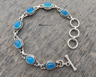 May include: A silver bracelet with a blue gemstone charm. The bracelet has a toggle clasp and is made of sterling silver.