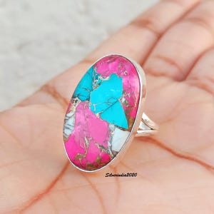 May include: A silver ring with an oval shaped turquoise and pink gemstone. The gemstone has a unique pattern of turquoise, pink, and white.