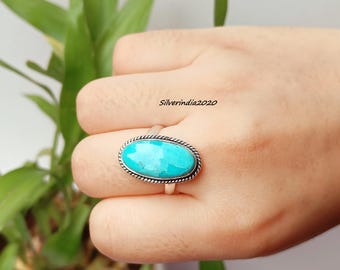 May include: A silver ring with an oval turquoise stone. The stone is surrounded by a twisted rope design. The ring is on a hand, with the text "Silverindia2020" visible.