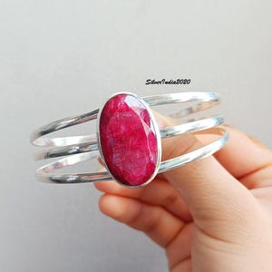 Puede incluir: Un brazalete de plata con tres bandas y una gran piedra preciosa ovalada de rubí engastada en el centro.