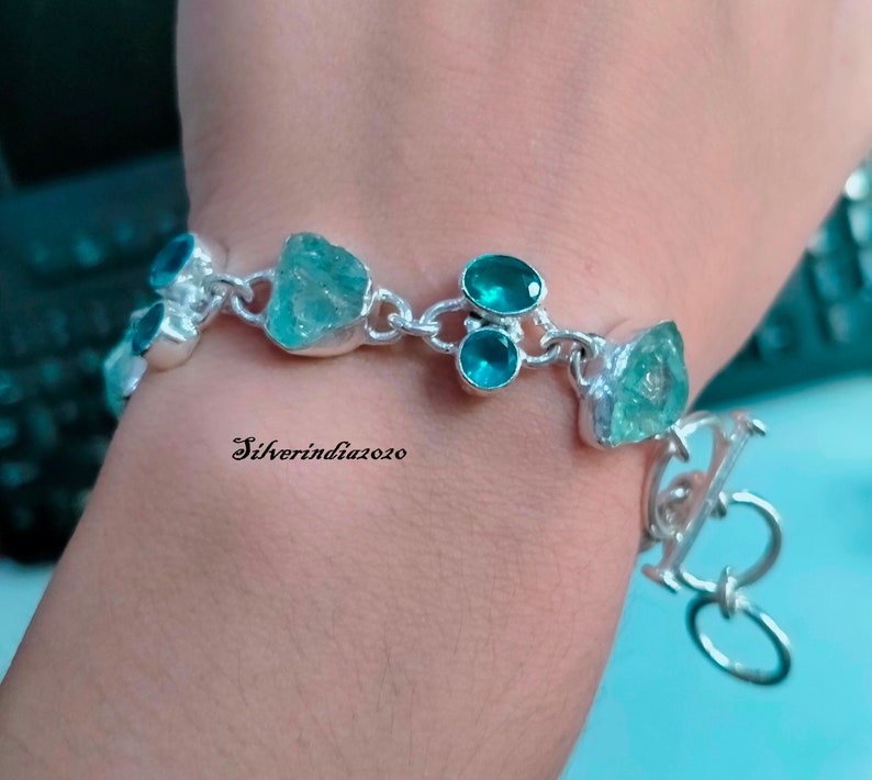 Puede incluir: Una pulsera de plata con una cadena y un cierre. La pulsera tiene varias piedras turquesa y azul claro.