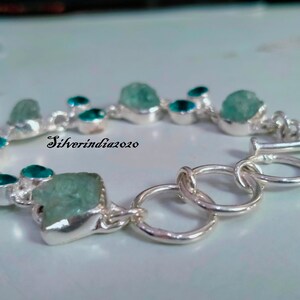Puede incluir: Un brazalete de plata con cierre de broche presenta una fila de piedras preciosas azul claro y turquesa. El brazalete est&aacute; hecho con una cadena de plata y tiene un broche de plata.