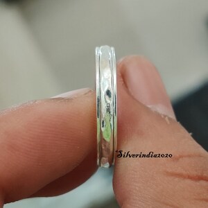 May include: A silver ring with a hammered texture and a smooth, polished band. The ring is shown on a finger.