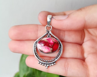 May include: A silver pendant with a teardrop design. The pendant features a large, oval-shaped stone with a vibrant red and pink pattern. The stone is set within a decorative silver frame with a twisted rope-like border and small beaded accents.