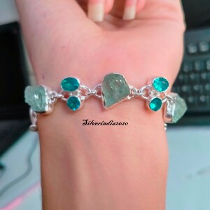 Puede incluir: Un brazalete de plata con un dise&ntilde;o de cadena presenta m&uacute;ltiples piedras preciosas de color azul claro y turquesa. El brazalete est&aacute; en la mu&ntilde;eca de una persona.