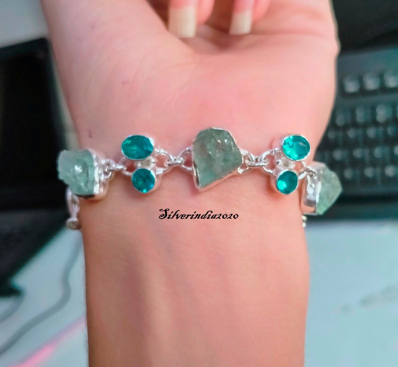 Puede incluir: Un brazalete de plata con un dise&ntilde;o de cadena presenta m&uacute;ltiples piedras preciosas de color azul claro y turquesa. El brazalete est&aacute; en la mu&ntilde;eca de una persona.