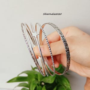 May include: Several silver bangles with different patterns. One bangle has a star-shaped design, others have floral and textured details. The bangles are displayed against a plain backdrop, with the text "Silverindia2020" visible.