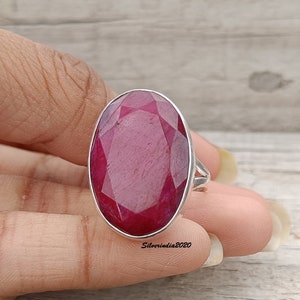 Pode incluir: Um anel de prata com uma grande pedra preciosa de rubi de corte oval. O rubi &eacute; de cor vermelha profunda e est&aacute; engastado numa banda de prata polida. O anel &eacute; uma pe&ccedil;a de joalharia marcante.