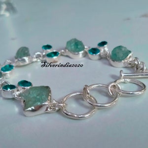 Puede incluir: Un brazalete de plata con cierre de palanca presenta un dise&ntilde;o de cadena con m&uacute;ltiples piedras preciosas azul aguamarina. Las piedras preciosas tienen una forma irregular y un aspecto &aacute;spero y natural. El brazalete est&aacute; acentuado con piedras preciosas m&aacute;s peque&ntilde;as, redondas, azul turquesa.