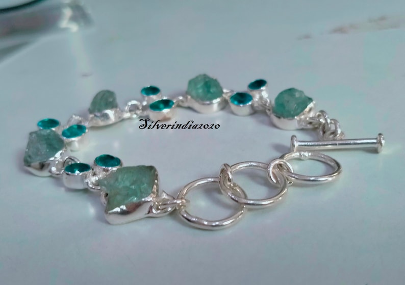 Puede incluir: Un brazalete de plata con cierre de palanca presenta un dise&ntilde;o de cadena con m&uacute;ltiples piedras preciosas azul aguamarina. Las piedras preciosas tienen una forma irregular y un aspecto &aacute;spero y natural. El brazalete est&aacute; acentuado con piedras preciosas m&aacute;s peque&ntilde;as, redondas, azul turquesa.