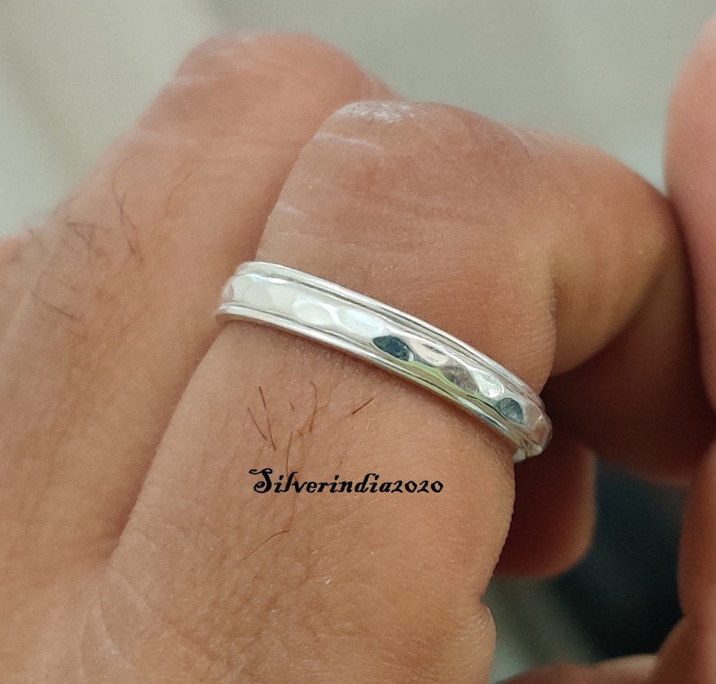 May include: A silver hammered band ring. The ring is worn on a finger.