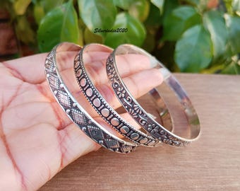 May include: Three silver bangles with intricate designs. The bangles are stacked on top of each other and have a polished finish.