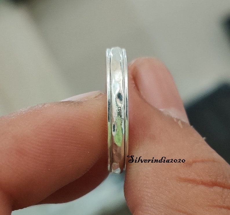 May include: A silver ring with a hammered texture and a smooth, polished band. The ring is shown on a finger.