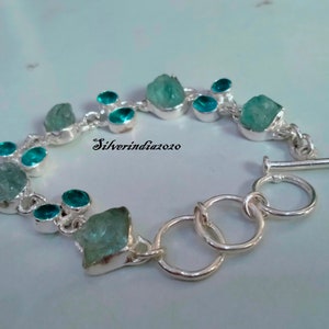 Puede incluir: Un brazalete de plata con cierre de palanca presenta una fila de piedras de aguamarina azul claro y piedras redondas turquesa m&aacute;s peque&ntilde;as.