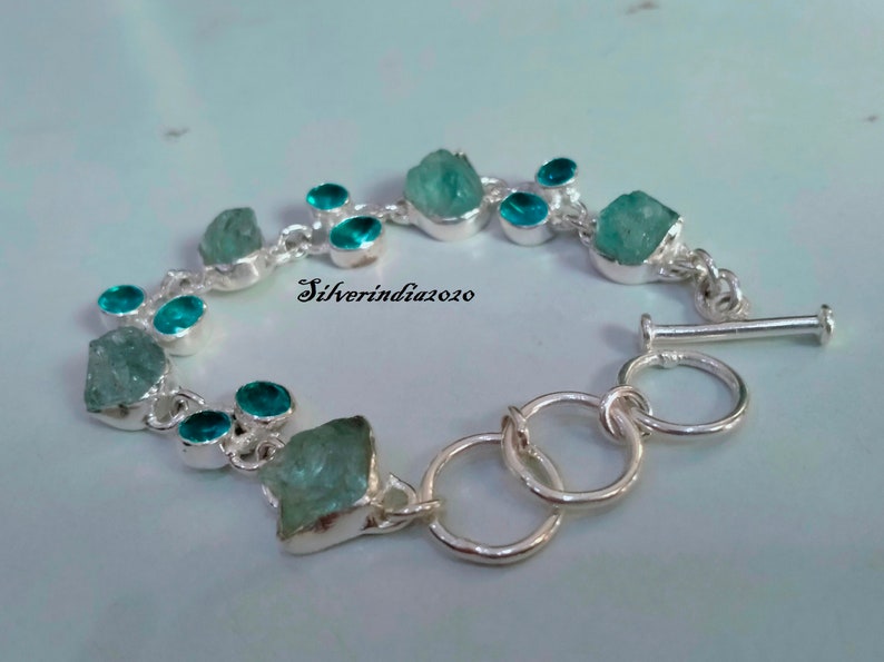 Puede incluir: Un brazalete de plata con cierre de palanca presenta una fila de piedras de aguamarina azul claro y piedras redondas turquesa m&aacute;s peque&ntilde;as.