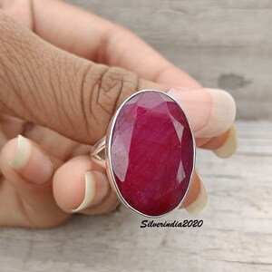 Pode incluir: Anel de prata com uma grande gema de rubi oval. O rubi &eacute; de um vermelho intenso e profundo. O anel &eacute; mostrado em uma m&atilde;o, destacando o tamanho e a cor da pedra preciosa.