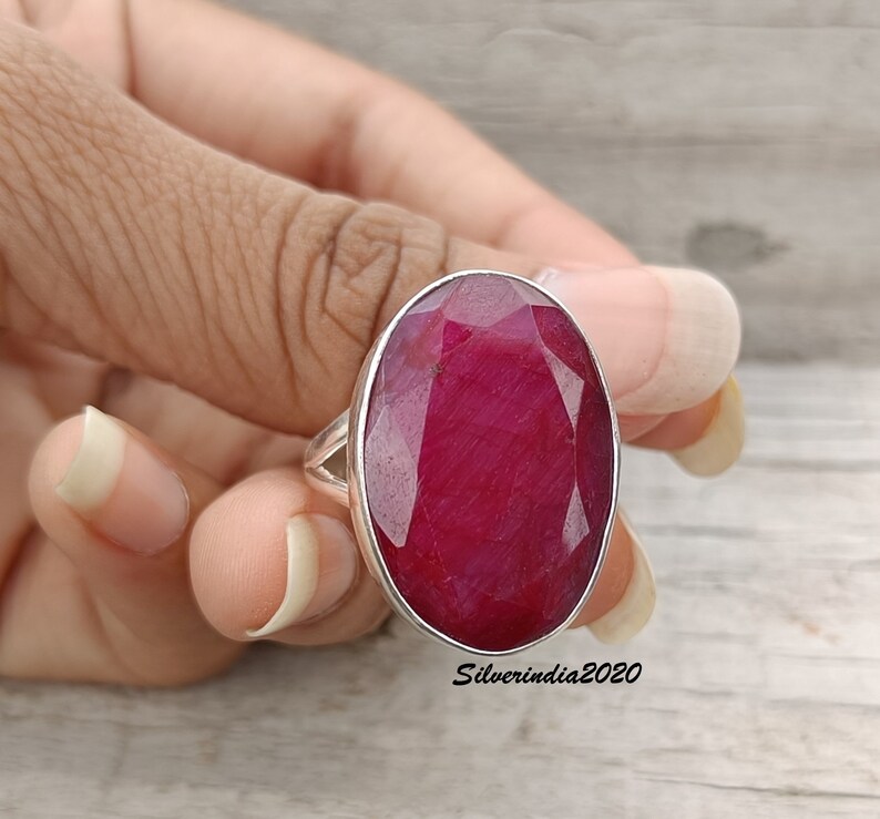 Pode incluir: Anel de prata com uma grande gema de rubi oval. O rubi &eacute; de um vermelho intenso e profundo. O anel &eacute; mostrado em uma m&atilde;o, destacando o tamanho e a cor da pedra preciosa.