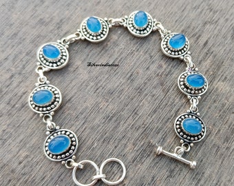 May include: A silver bracelet with blue oval stones set in a beaded frame. The bracelet has a toggle clasp.