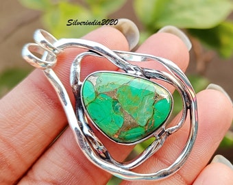 May include: A handcrafted silver pendant featuring a vibrant green and gold stone. The stone is set within a unique, swirling silver frame. The pendant has a loop for a chain. The text "Silverindia2020" is visible.